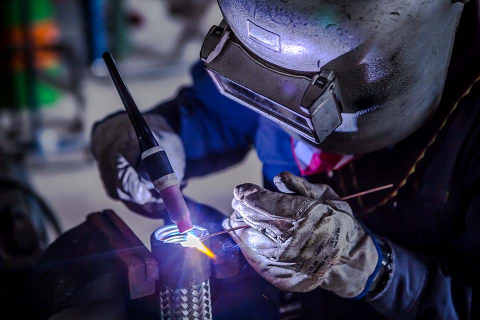 Welder is welding Tungsten Inert Gas welding, TIG weld for making new stainless flexible hose in manufacturer workshop / TIG welding torch