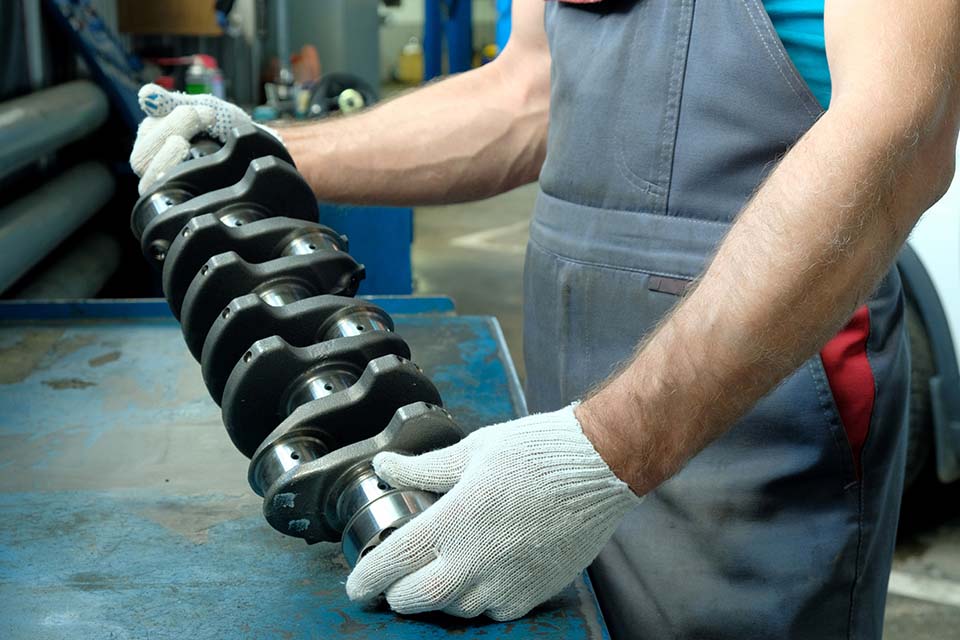 In the hands of a car mechanic, a new crankshaft. Car engine repair. The quality of the spare part is checked before it is installed.